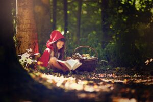Menina fantasiada de Chapeuzinho Vermelho lendo um livro na floresta