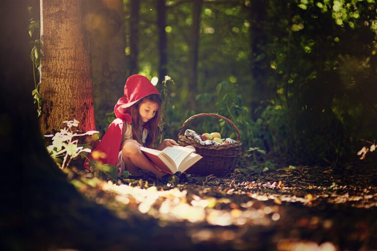 Menina fantasiada de Chapeuzinho Vermelho lendo um livro na floresta